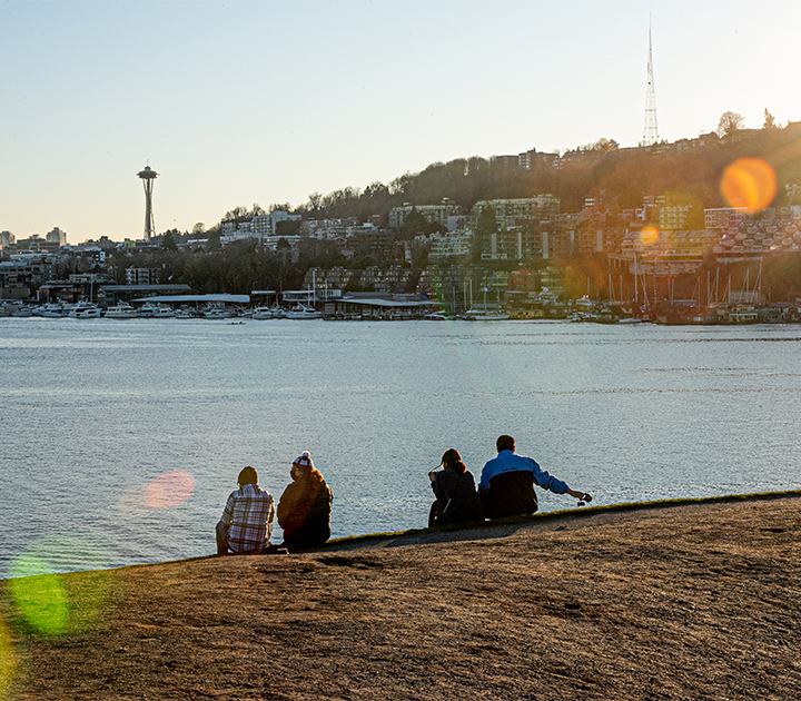People sitting at the shore of Lake Union, with the Space Needle in the distance.
