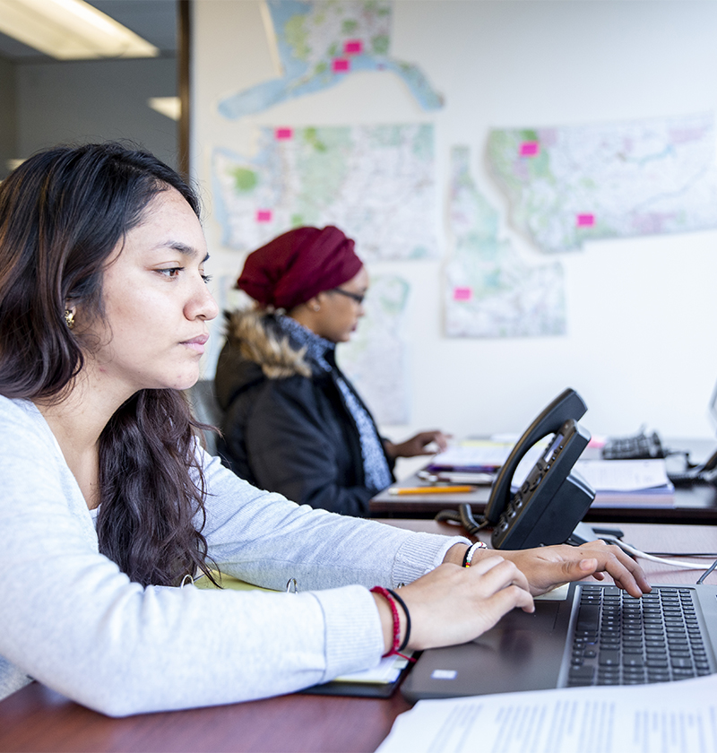 A student sits at a desk and is typing at her computer.