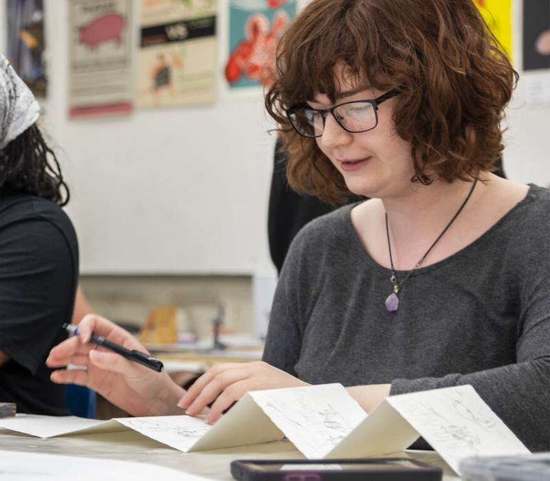 Female student with glasses drawing on paper in front of her