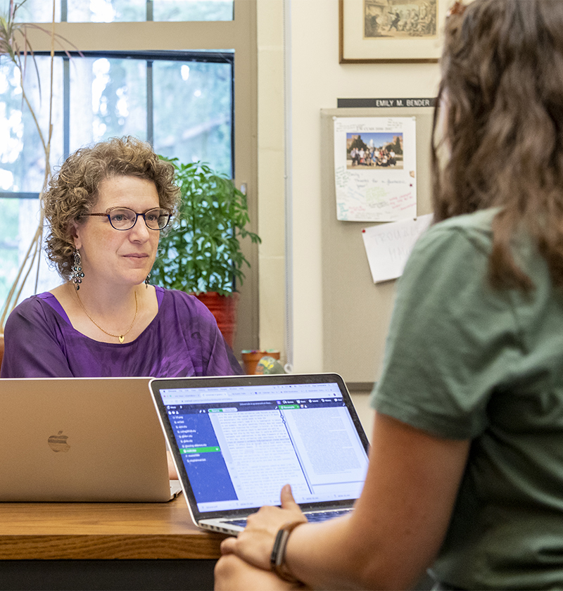 Female teacher in office with laptop talking to student with laptop