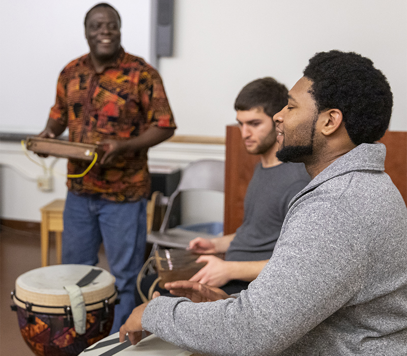 Student drumming, other student and teacher in background