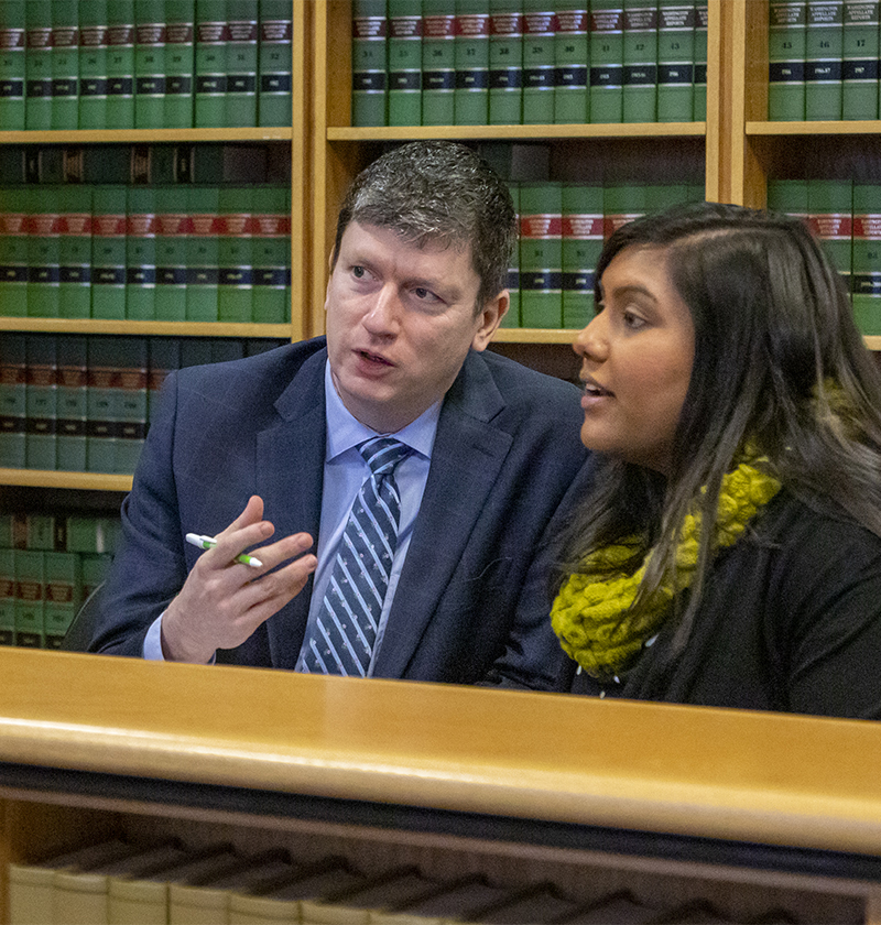 Man in suit in front of books talking with female both sitting