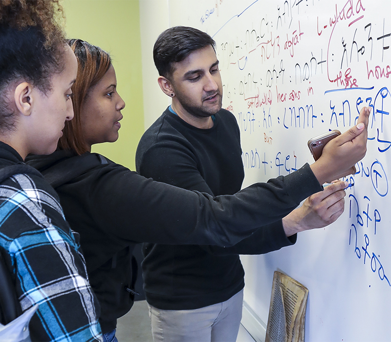 Male teacher gesturing to white board with two students