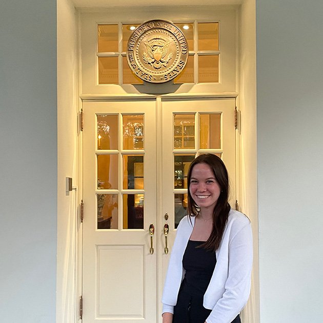 Student standing outside a government office with official seal over the door.