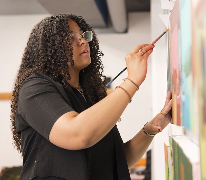 Kyra Wolfenbarger standing and painting in an art studio.