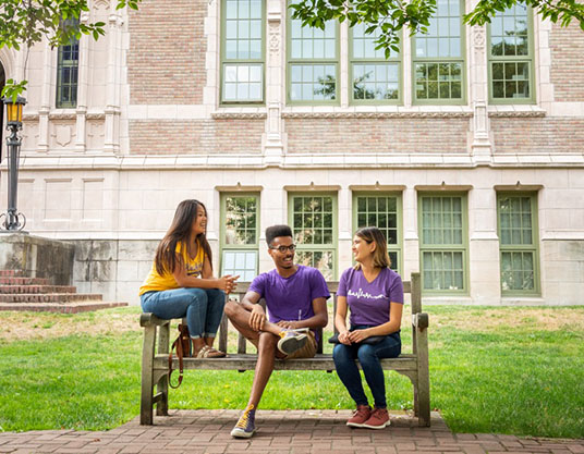 Three students sitting on outdoor bench on UW Seattle campus