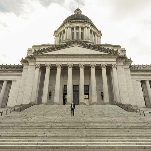 Man in suit standing in front of the Capitol building in Olympia on the stairs