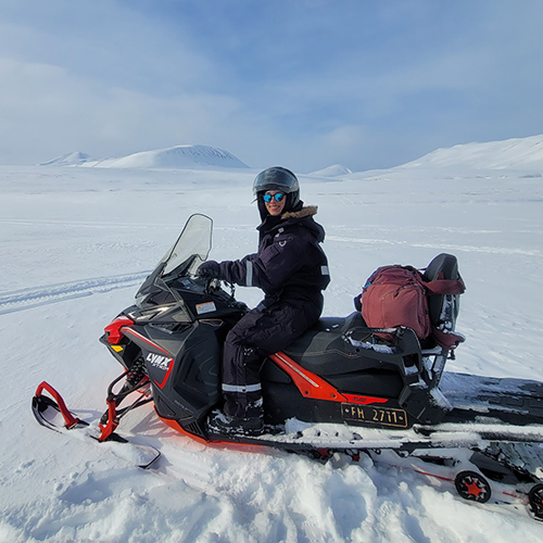 Mia Bennett on a snowmobile with a vast snowy arctic landscape behind her.